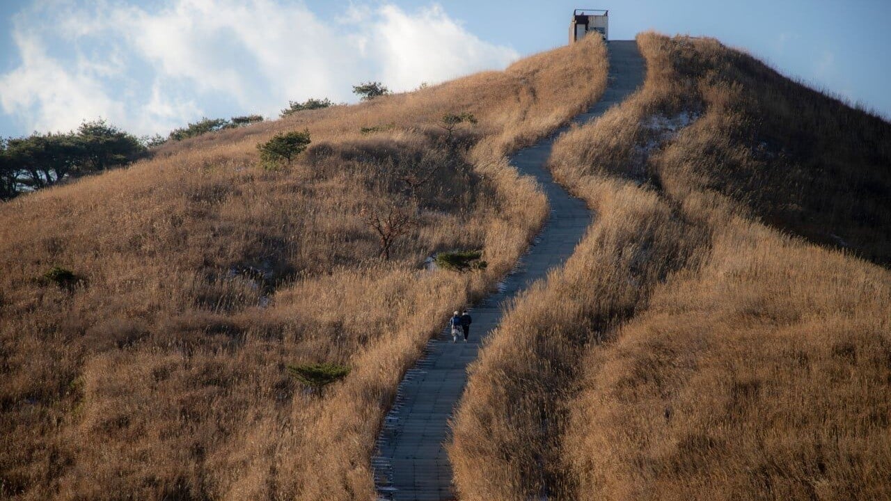 A curving path climbing toward a small facility on a Hwangmaesan ridge